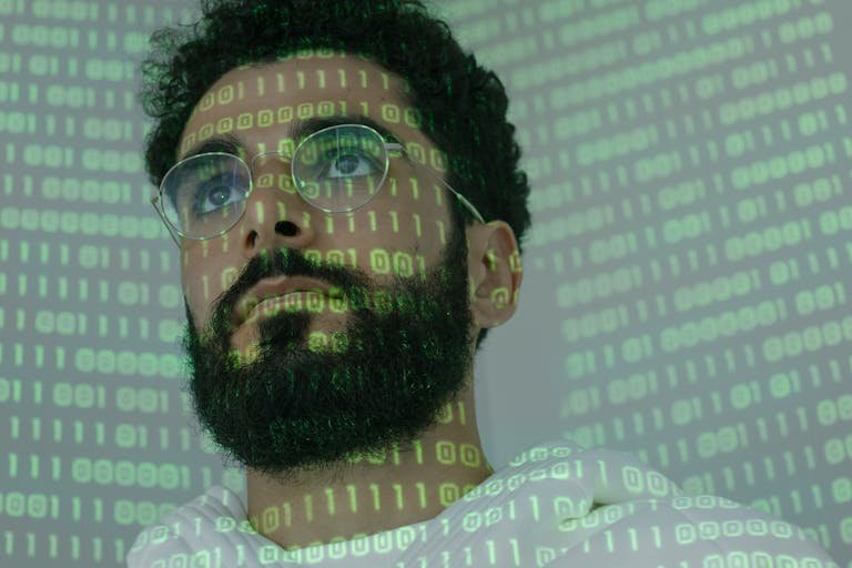 Close-up of a man with glasses and binary code projection, symbolizing cyber security. Photo by cottonbro studio