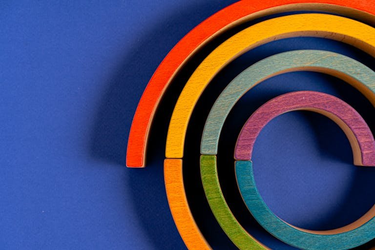 Vibrant wooden rainbow toy pieces arranged against a blue backdrop.